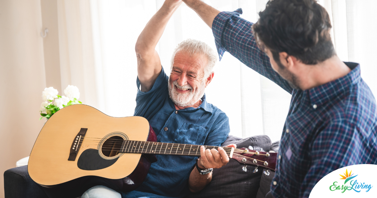 A smiling son high fives his happy elderly father as he plays the guitar, showing the positive effect music can have on people, including those with dementia.